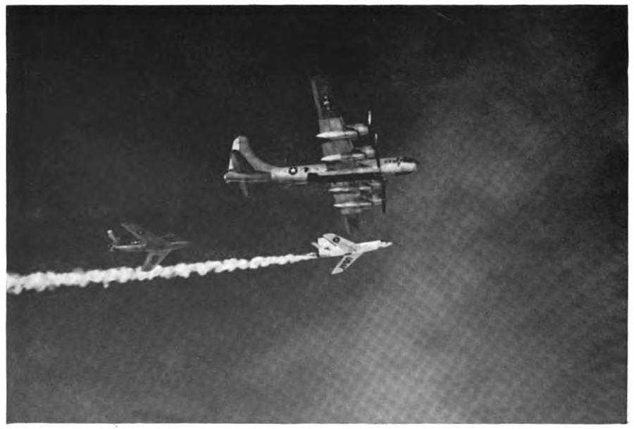 Three planes in the air, one small one with a large contrail directly below a larger plane