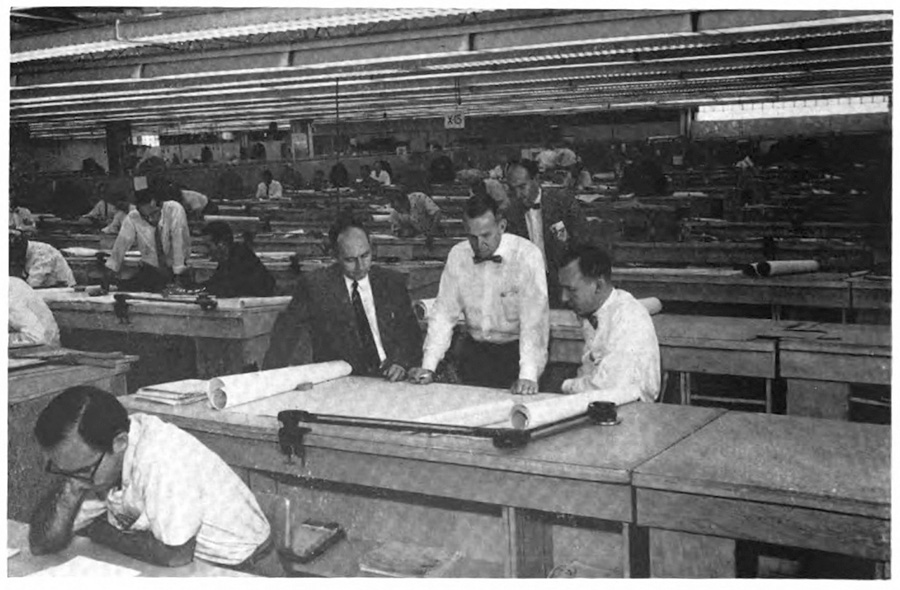 A large room full of workers studying diagrams at their desks