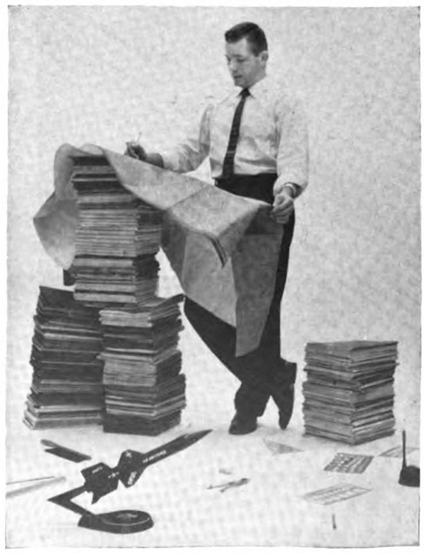 A man standing next to three large piles of reports, the tallest of which is above his waist