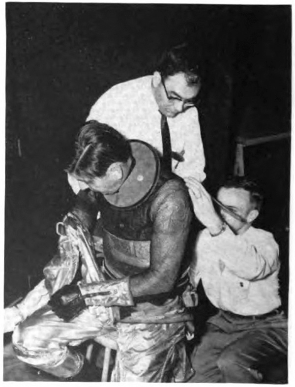 A man putting on a pressure suit with two men assisting