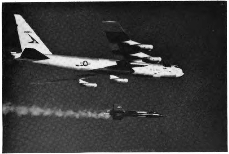 A plane in the air with a smaller plane directly beneath it; the smaller plane is clear of the larger plane and has a large contrail