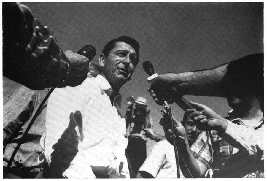 A man standing in front of several people who are holding out microphones to him