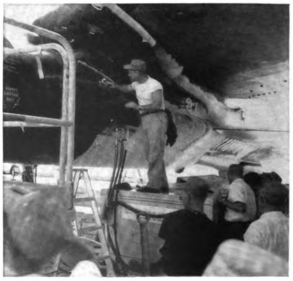 A man standing on a ladder inspecting a small plane attached to a larger plane